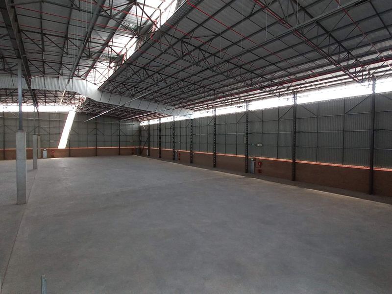 A spacious, open-plan industrial warehouse featuring high ceilings with exposed steel trusses, concrete flooring, and natural light provided by integrated skylights.