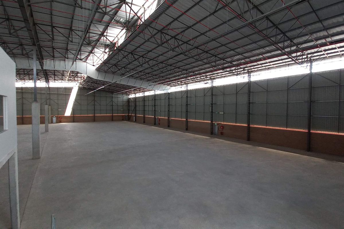 A spacious, open-plan industrial warehouse featuring high ceilings with exposed steel trusses, concrete flooring, and natural light provided by integrated skylights.