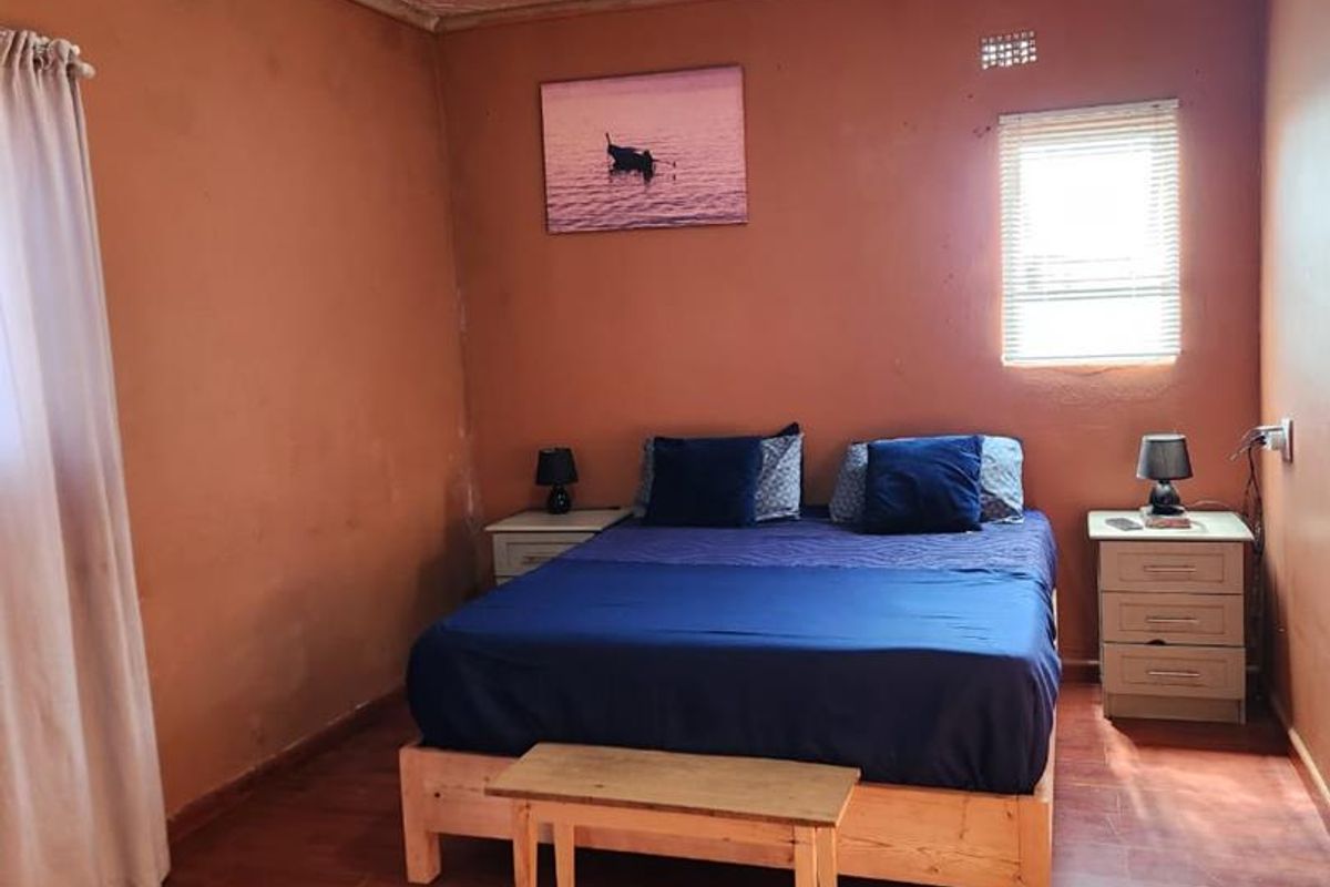 A bedroom featuring wood-look flooring, a textured ceiling, and a window with blinds, providing a functional sleeping space.
