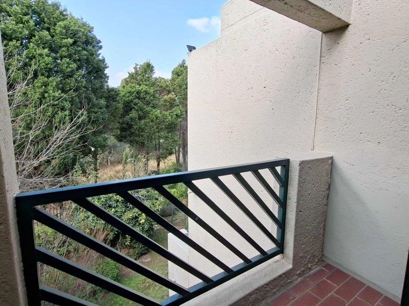 A private balcony featuring a metal balustrade and tiled flooring, offering a view of the surrounding trees and greenery.