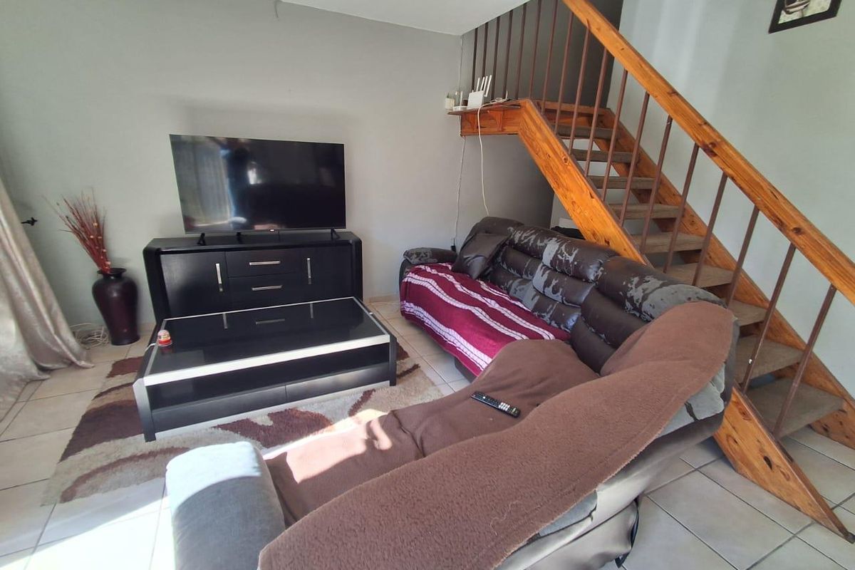 A living room area featuring tiled flooring and an open-plan staircase with wooden treads and a metal railing.