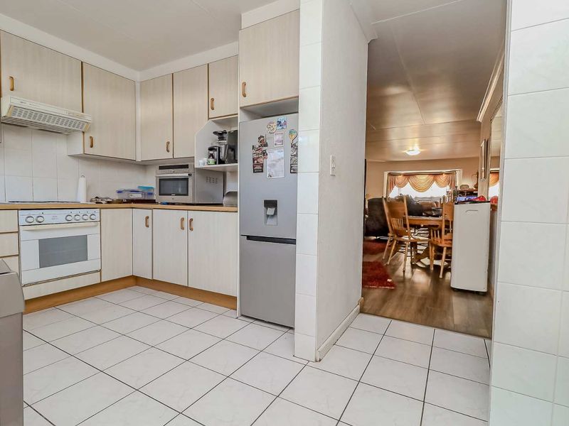 A functional kitchen featuring light-toned cabinetry, tiled flooring, and a built-in oven, with an open-plan flow leading into the adjacent living and dining area.