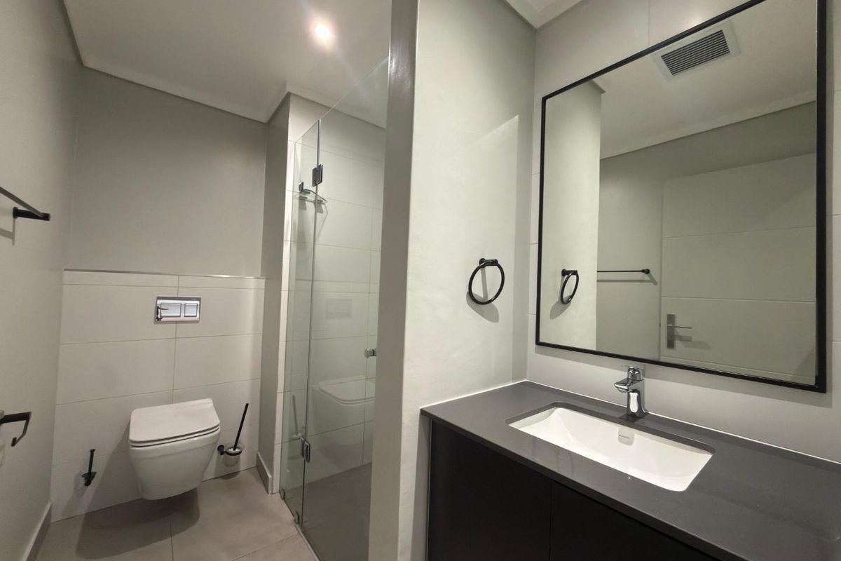 Modern bathroom featuring a wall-mounted toilet, glass-enclosed shower, and a sleek vanity with a dark countertop and framed mirror.