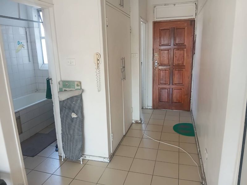 A functional apartment hallway featuring tiled flooring, built-in storage cupboards, and a solid timber entrance door, providing access to the adjacent bathroom.