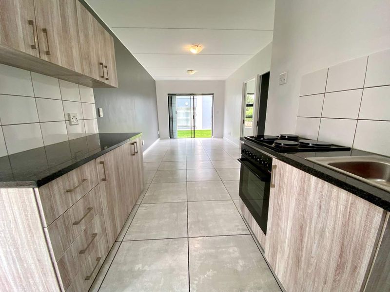 Open-plan kitchen and living area featuring modern laminate cabinetry, granite countertops, tiled flooring, and direct access to an outdoor space via sliding doors.
