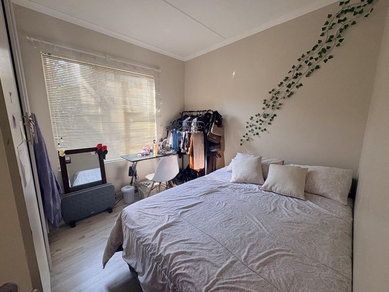 A functional bedroom featuring light-toned laminate flooring and a window fitted with venetian blinds.