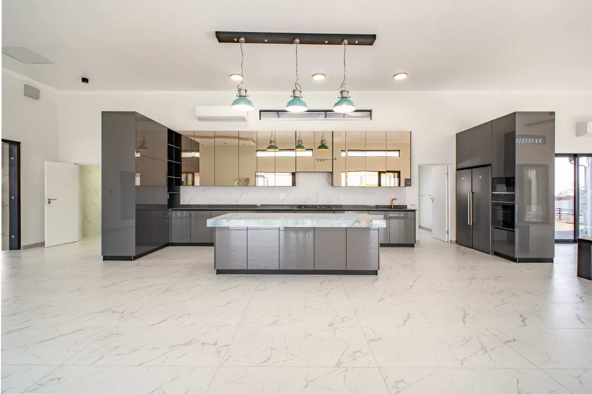 Modern open-plan kitchen featuring high-gloss grey cabinetry, a central marble-topped island, integrated appliances, and sleek marble-look floor tiles.