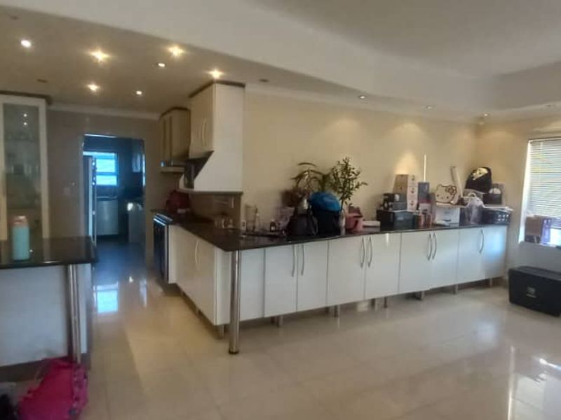 Spacious open-plan kitchen and living area featuring modern white cabinetry, granite countertops, recessed lighting, and tiled flooring throughout.