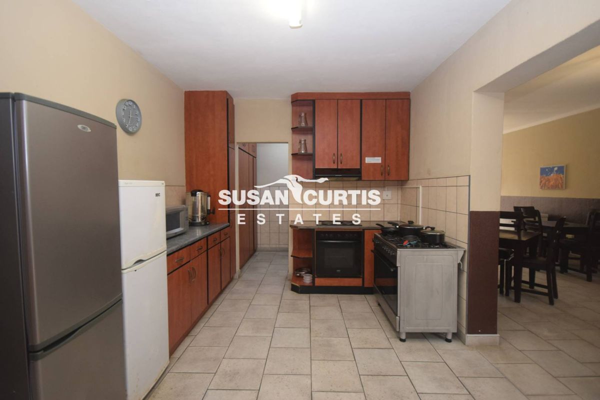 A functional kitchen featuring wooden cabinetry, tiled flooring, and a built-in oven with extractor fan, leading into an adjacent dining area.