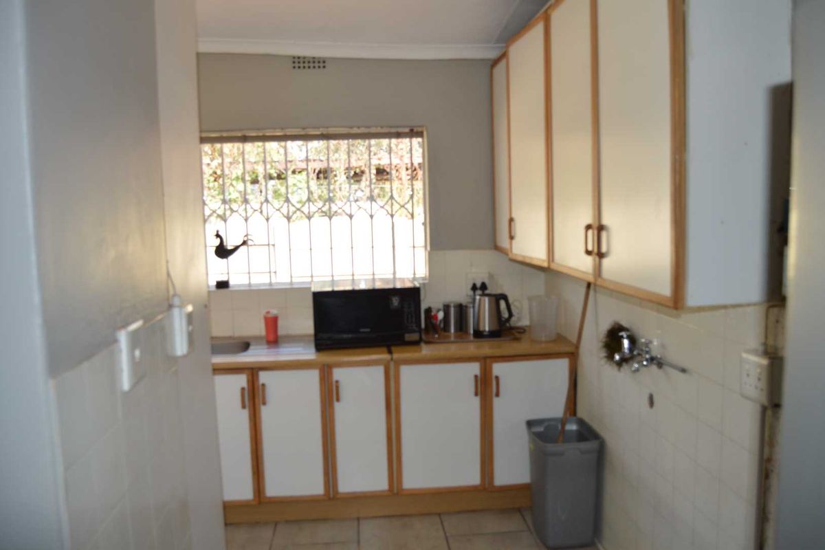 A functional kitchen area featuring built-in cabinetry, a stainless steel sink, and tiled splashbacks, providing a practical workspace for office staff.