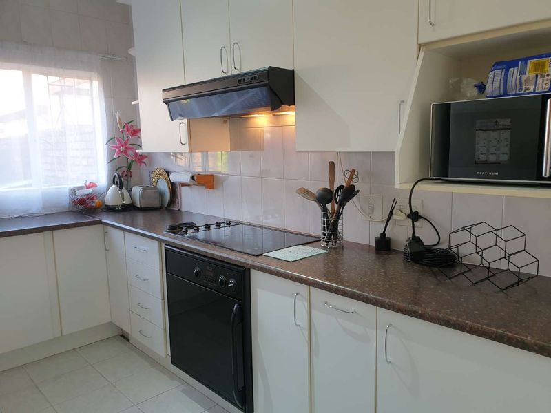 A functional kitchen featuring white cabinetry, dark laminate countertops, a built-in oven, electric hob, and tiled backsplash.