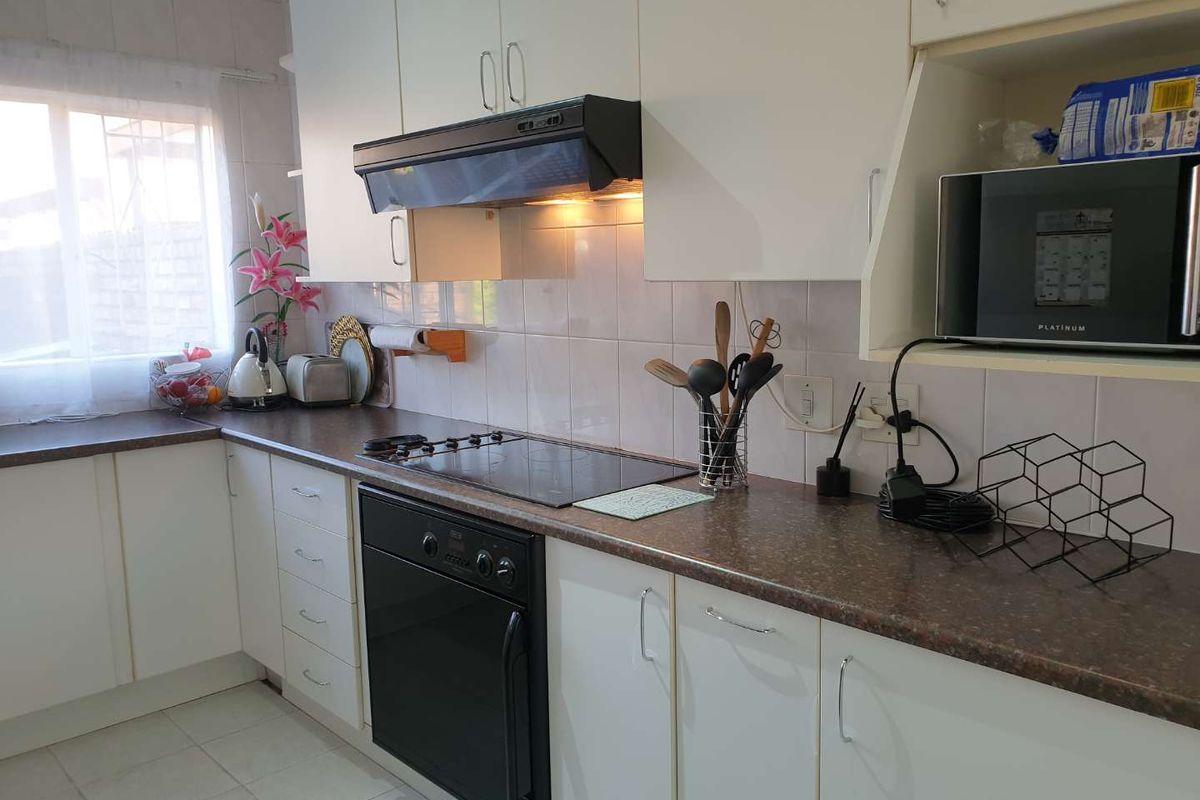 A functional kitchen featuring white cabinetry, dark laminate countertops, a built-in oven, electric hob, and tiled backsplash.