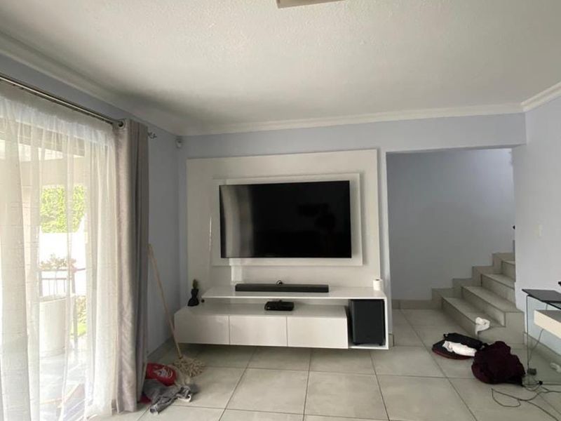 A bright living room featuring large format floor tiles, a modern built-in media console, and a sliding glass door leading to an outdoor area.