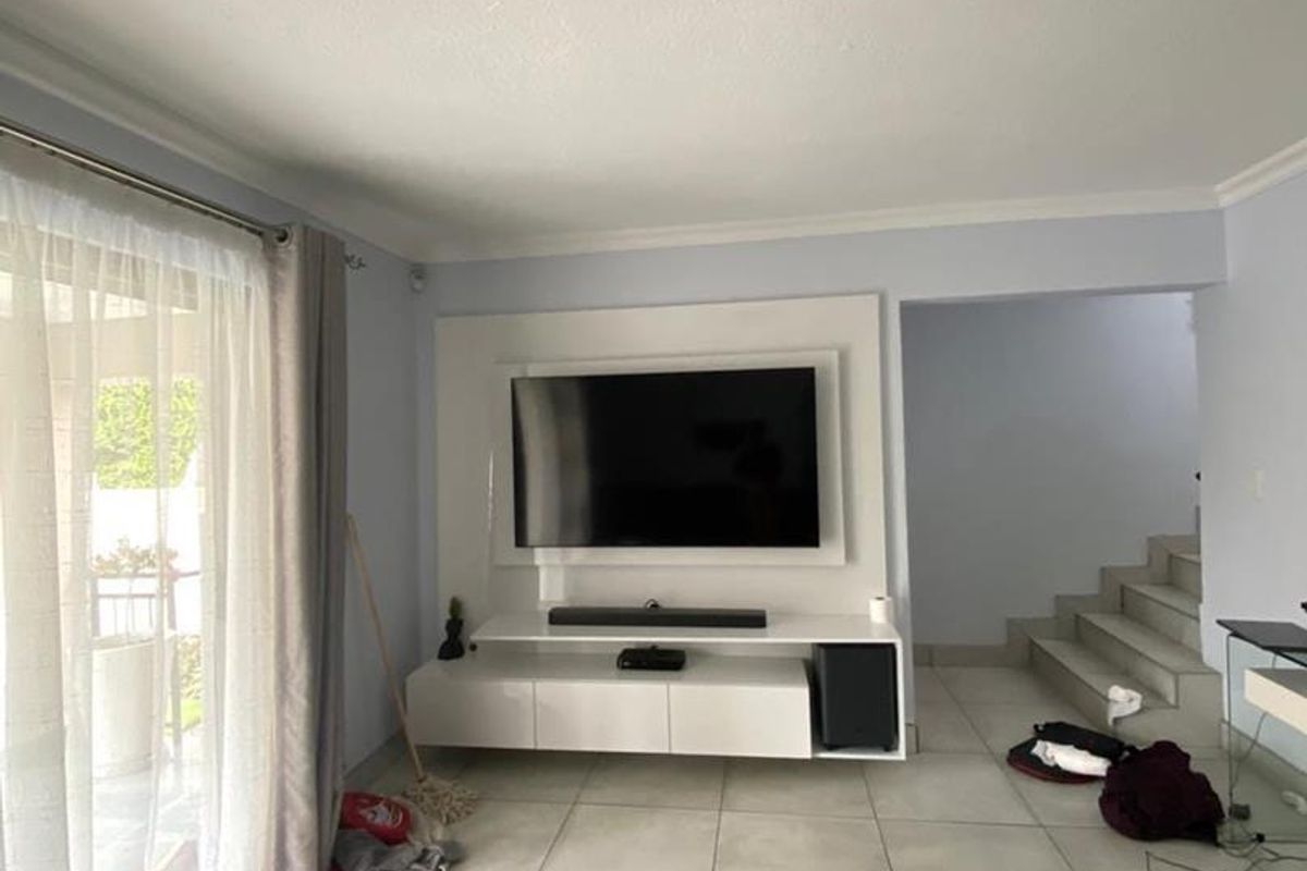 A bright living room featuring large format floor tiles, a modern built-in media console, and a sliding glass door leading to an outdoor area.