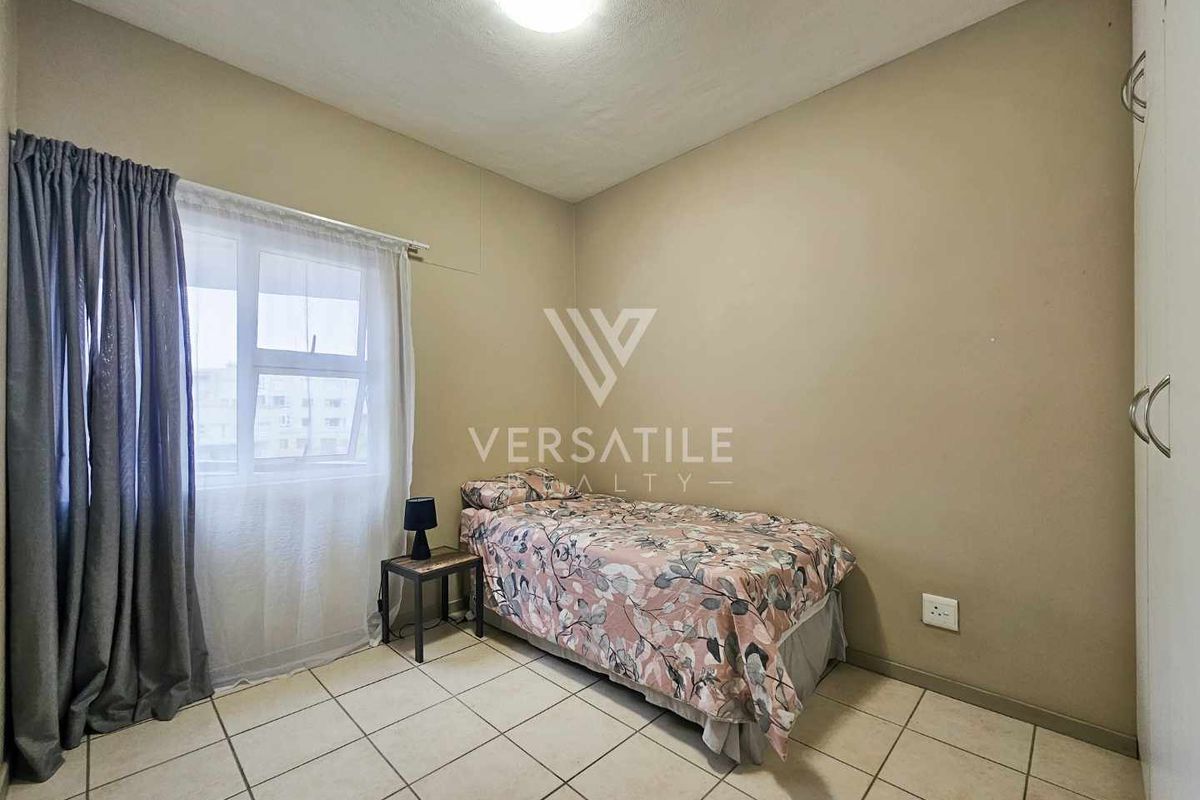 A functional bedroom featuring tiled flooring, built-in wardrobe storage, and a window with curtain tracks.