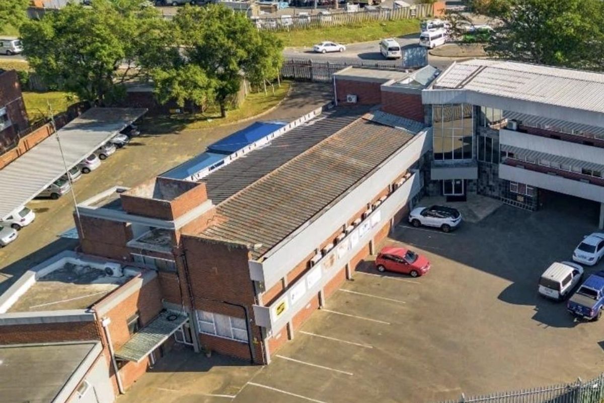 Aerial view of a commercial property featuring a brick building, asphalt parking area, and secure perimeter fencing.