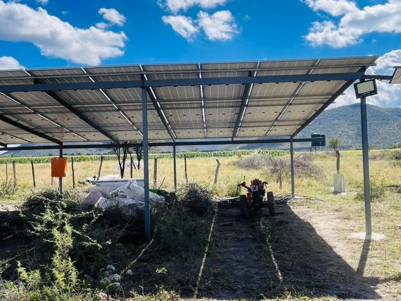 A large ground-mounted solar panel array providing shaded utility space on the farm, featuring a sturdy metal frame and integrated lighting.