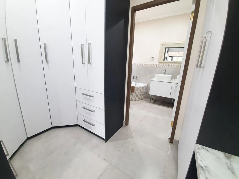A clean, modern bedroom dressing area featuring extensive built-in cabinetry and tiled flooring, with direct access to an en-suite bathroom.