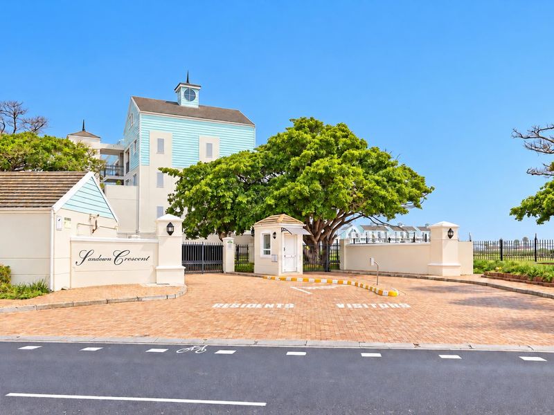 The entrance to Sandown Crescent apartment complex, featuring a secure gated access point, guard house, and well-maintained paved driveway.