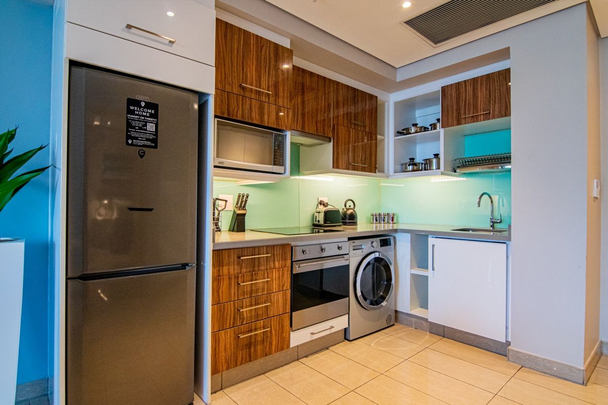 Modern compact kitchen featuring wood-grain cabinetry, integrated oven, hob, extractor fan, built-in microwave, and a convenient under-counter washing machine.