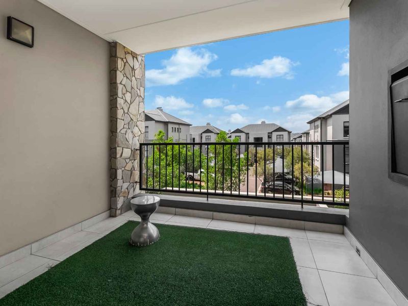 A modern covered balcony featuring tiled flooring, stone accent wall, and a metal balustrade, offering a pleasant outdoor space for relaxation.