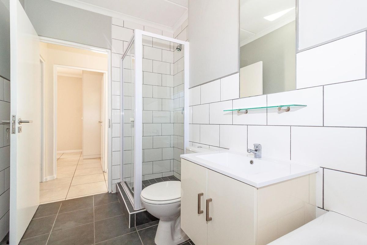 A clean, modern bathroom featuring a glass shower enclosure, vanity cabinet with basin, and neutral wall and floor tiling.