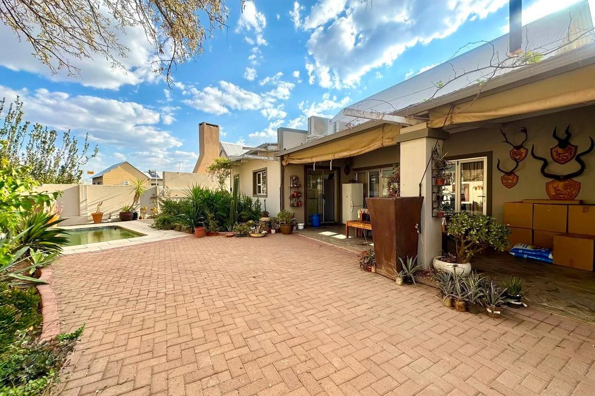 Rear exterior view featuring a paved patio area, covered veranda, and a swimming pool set within a landscaped garden.