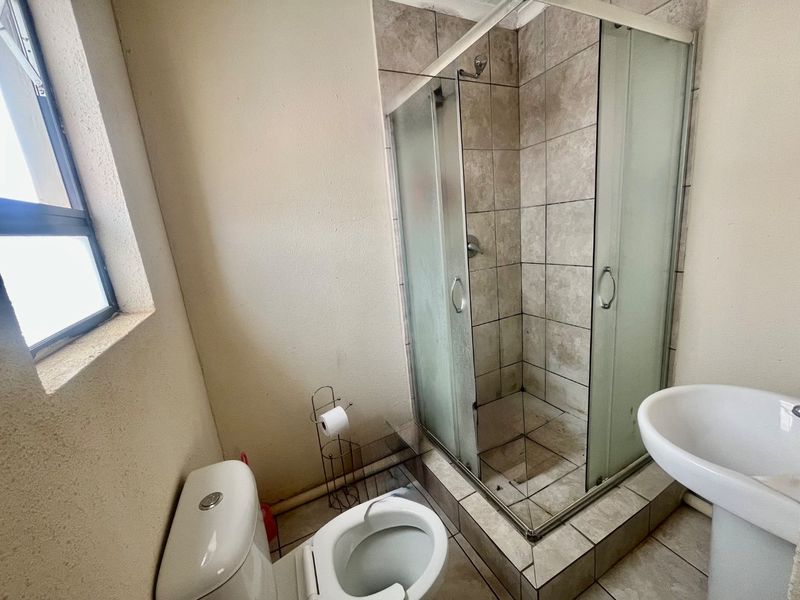Compact bathroom featuring a tiled shower enclosure, pedestal basin, and toilet. The space would benefit from a refresh of the tiling and fixtures.