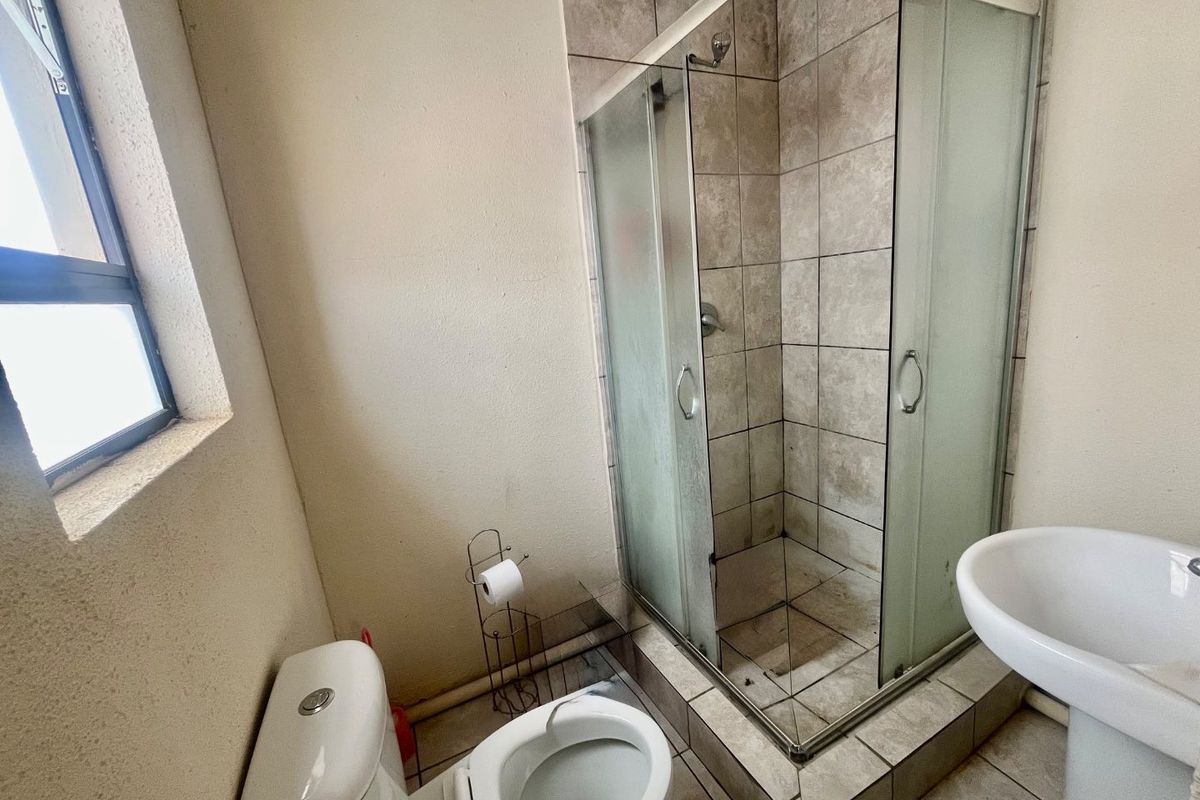 Compact bathroom featuring a tiled shower enclosure, pedestal basin, and toilet. The space would benefit from a refresh of the tiling and fixtures.
