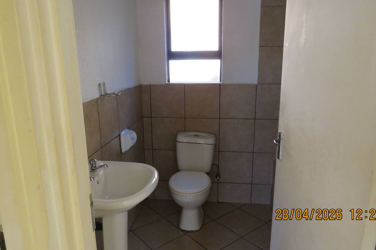 A functional guest bathroom featuring a pedestal basin, a standard toilet, and neutral wall and floor tiling.