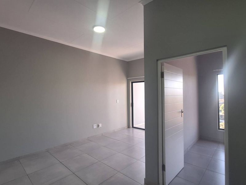 An empty, modern living area featuring neutral grey walls, tiled flooring, and a sliding glass door leading to an outdoor space.