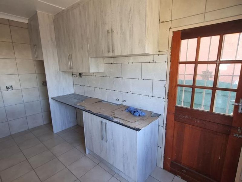 A kitchen area currently undergoing renovation, featuring new cabinetry and partially installed wall tiles, awaiting final finishes and grouting.