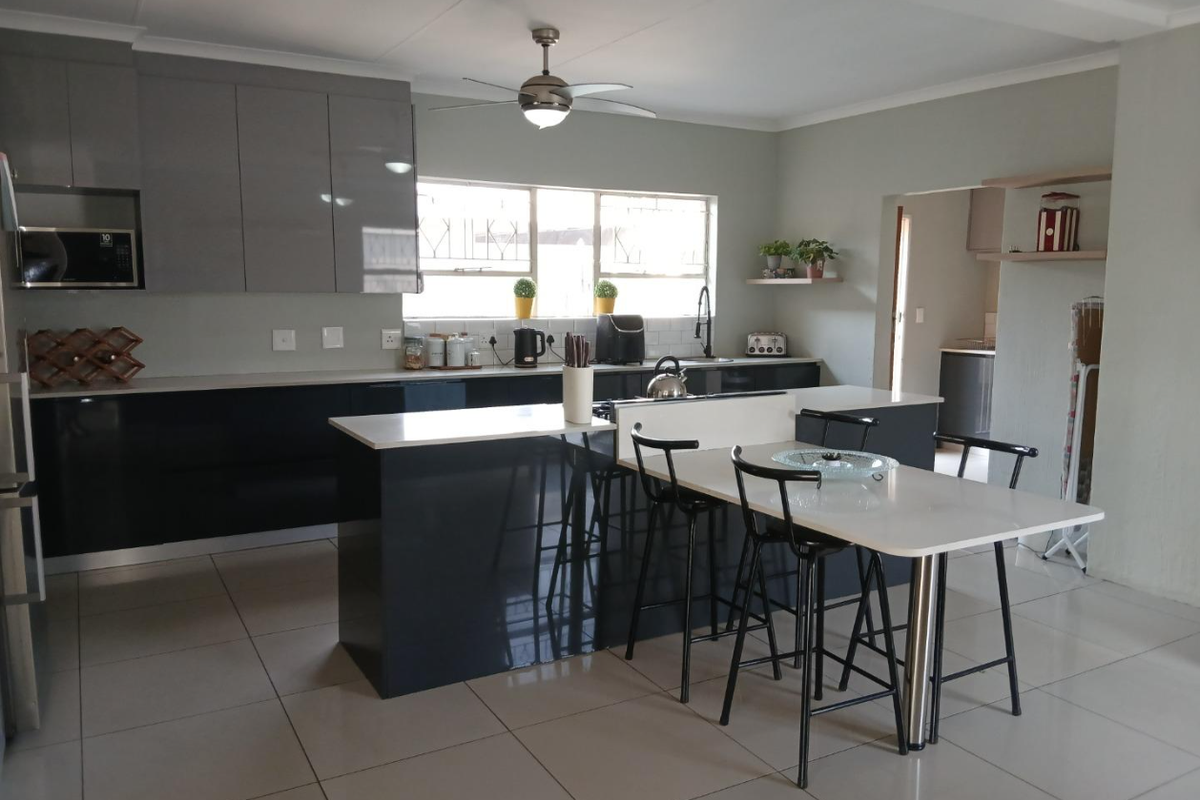 Modern kitchen featuring sleek dark cabinetry, a central island with an integrated breakfast bar, tiled flooring, and a built-in microwave.