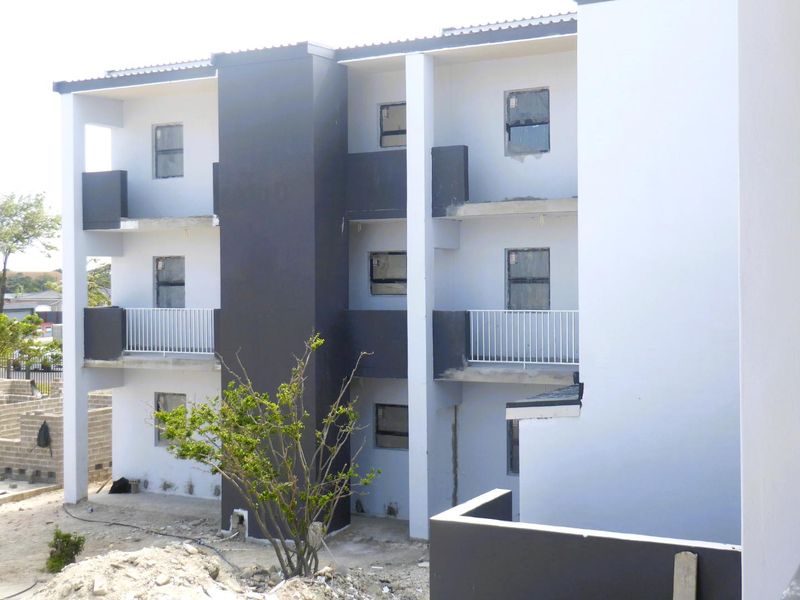 Rear elevation of a modern apartment building featuring multiple balconies with metal railings and clean architectural lines, currently in the final stages of construction.
