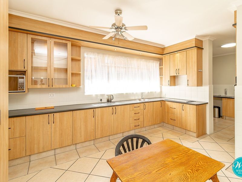 A functional kitchen featuring light wood-finish cabinetry, dark countertops, tiled flooring, and a built-in hob, with an adjacent scullery area visible.
