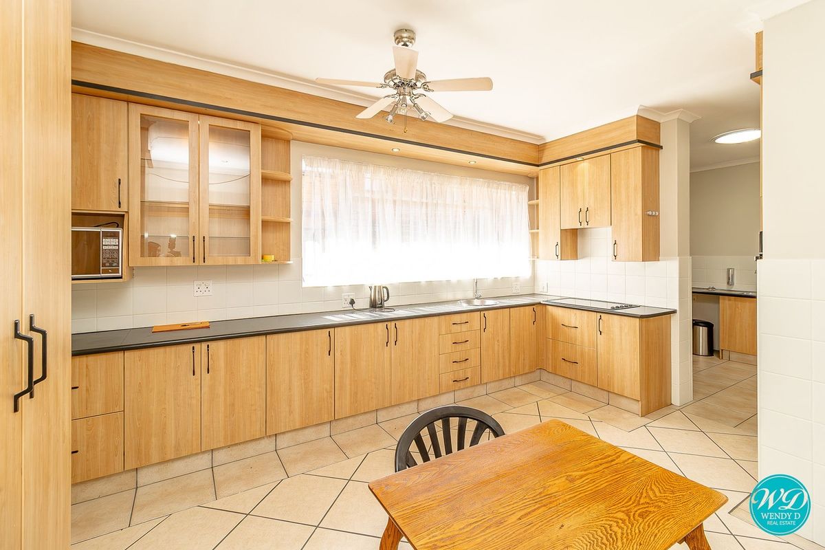 A functional kitchen featuring light wood-finish cabinetry, dark countertops, tiled flooring, and a built-in hob, with an adjacent scullery area visible.