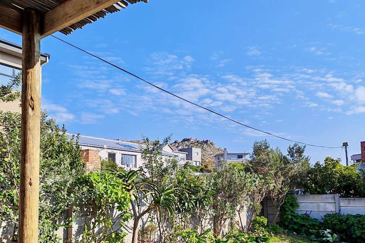 A view of the rear garden featuring a timber pergola structure, established greenery, and a concrete boundary wall under a clear blue sky.
