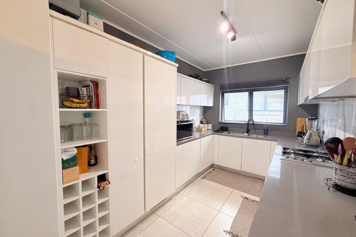 Modern kitchen featuring white high-gloss cabinetry, stone countertops, integrated storage, and a built-in gas hob with a sleek, functional layout.