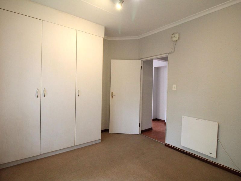 A clean, empty bedroom featuring built-in cupboards, neutral wall finishes, and a wall-mounted heater, providing a versatile space ready for personalization.
