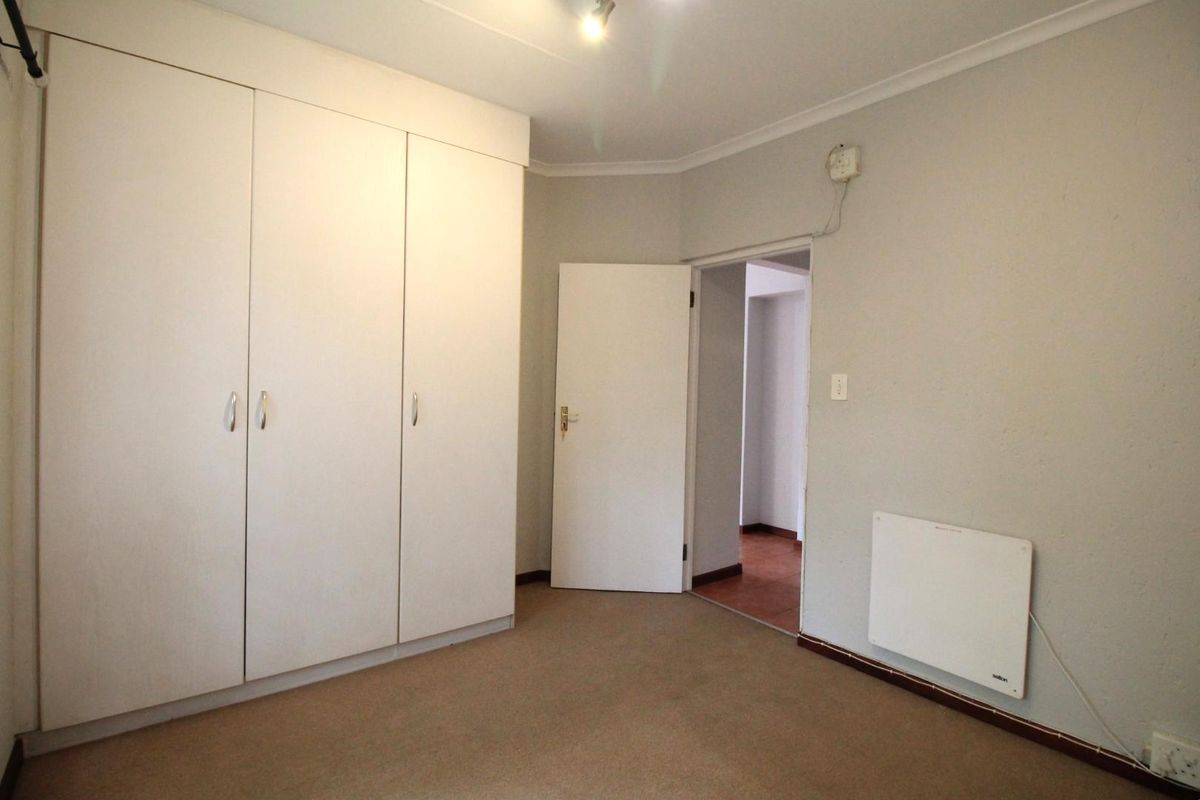A clean, empty bedroom featuring built-in cupboards, neutral wall finishes, and a wall-mounted heater, providing a versatile space ready for personalization.