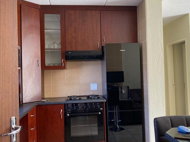 Compact kitchen featuring dark wood cabinetry, tiled backsplash, and integrated electric stove with extractor fan.
