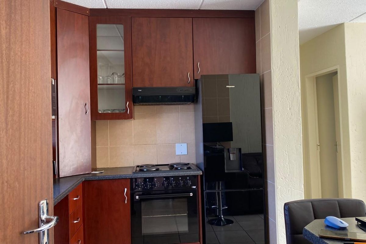 Compact kitchen featuring dark wood cabinetry, tiled backsplash, and integrated electric stove with extractor fan.