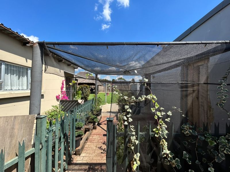 Rear outdoor area featuring a paved walkway, picket fencing, and overhead shade netting structure.