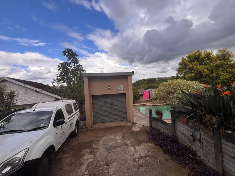 Exterior view of a detached garage with a roller door, adjacent to a swimming pool area and concrete driveway.