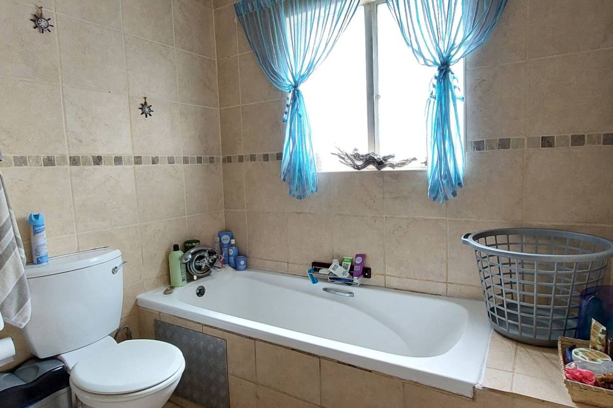 A functional bathroom featuring a built-in bathtub with tiled surround, a standard toilet, and wall-mounted fixtures.
