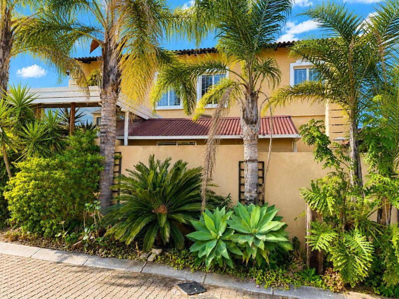 Front elevation of a two-story residential property featuring a stucco facade, tiled roof, and established garden landscaping with mature palm trees.