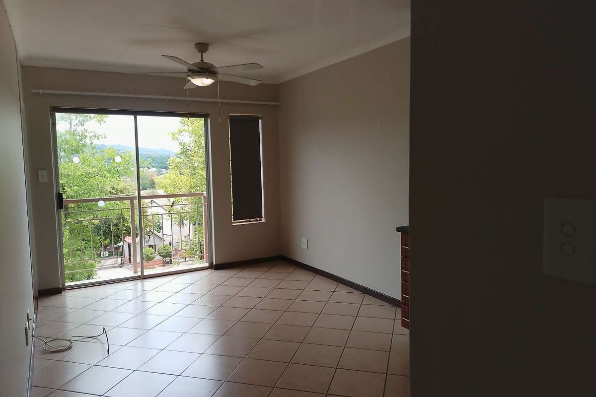 An empty living area featuring tiled flooring, a ceiling fan, and a sliding glass door leading to a balcony with neighborhood views.