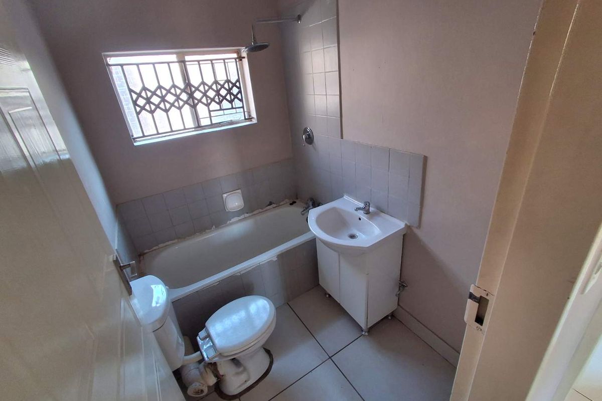 A compact bathroom featuring a bathtub with shower head, pedestal basin, and toilet, finished with tiled flooring and a security-fitted window.