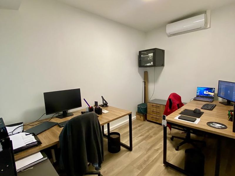 A functional office space featuring laminate wood flooring, a wall-mounted air conditioning unit, and a wall-mounted network cabinet.