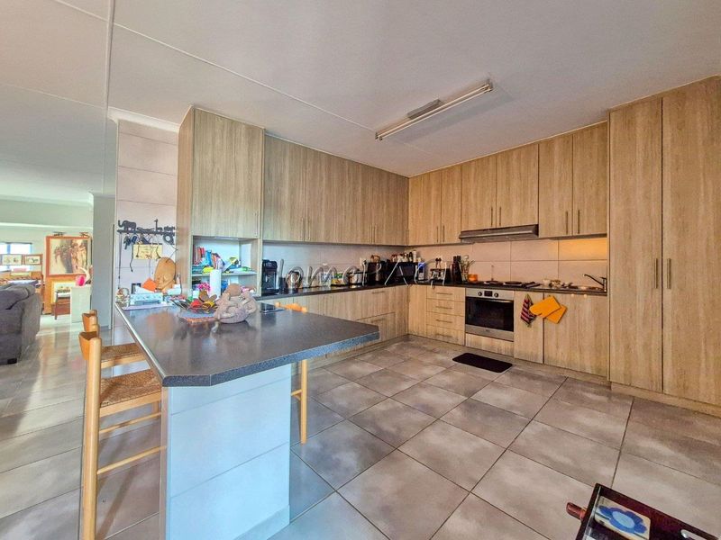 A functional kitchen featuring wood-look cabinetry, a central island, built-in oven, extractor fan, and tiled flooring, offering ample storage and workspace.